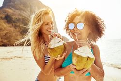 Two happy female friends drinking a tropical cocktail on the beach