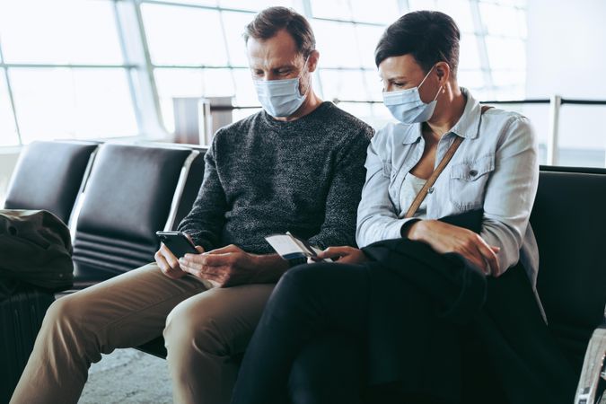 Couple wearing face masks checking phone for flight timing while waiting at gate