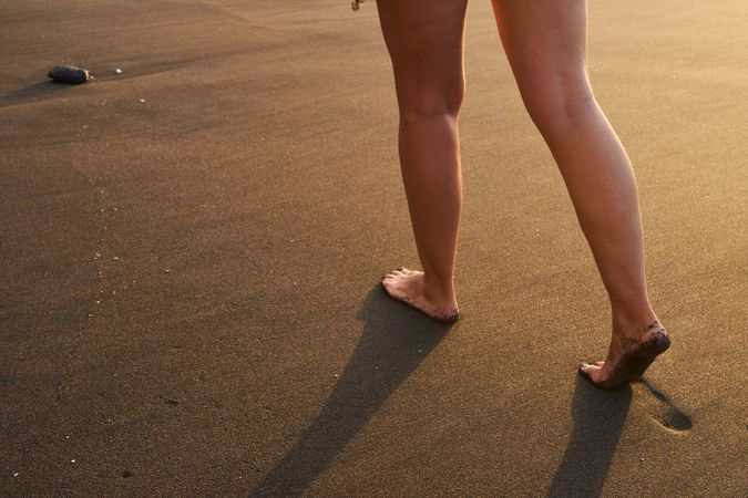 Crop woman strolling on sand of beach