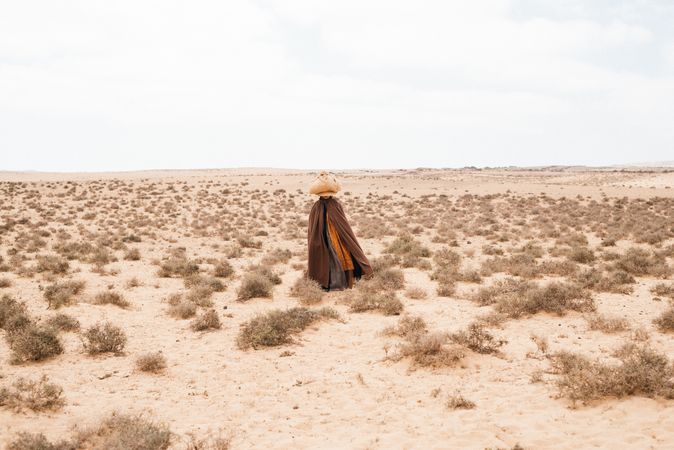 Woman in long robes walking through arid landscape with basket on head