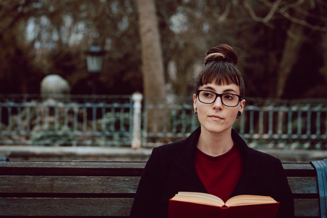 Young woman reading book on bench in park