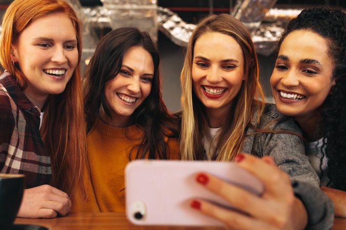 Woman sitting with friends at coffee shop making a selfie