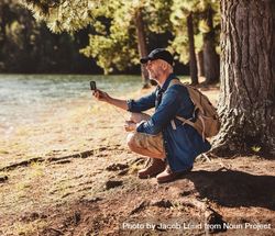 Portrait of mature man sitting near a lake using compass for searching direction 5wLwL4