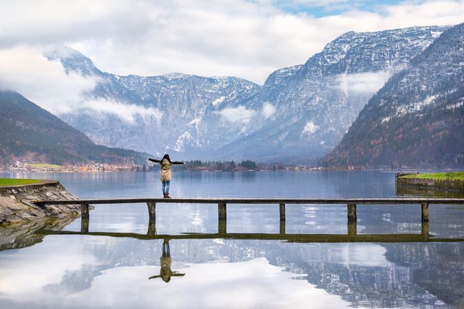 Woman stretching her arms out standing on a bridge over alpine lake