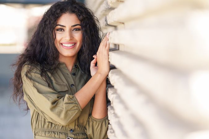 Smiling Middle Eastern woman resting on outside wall, with space for text