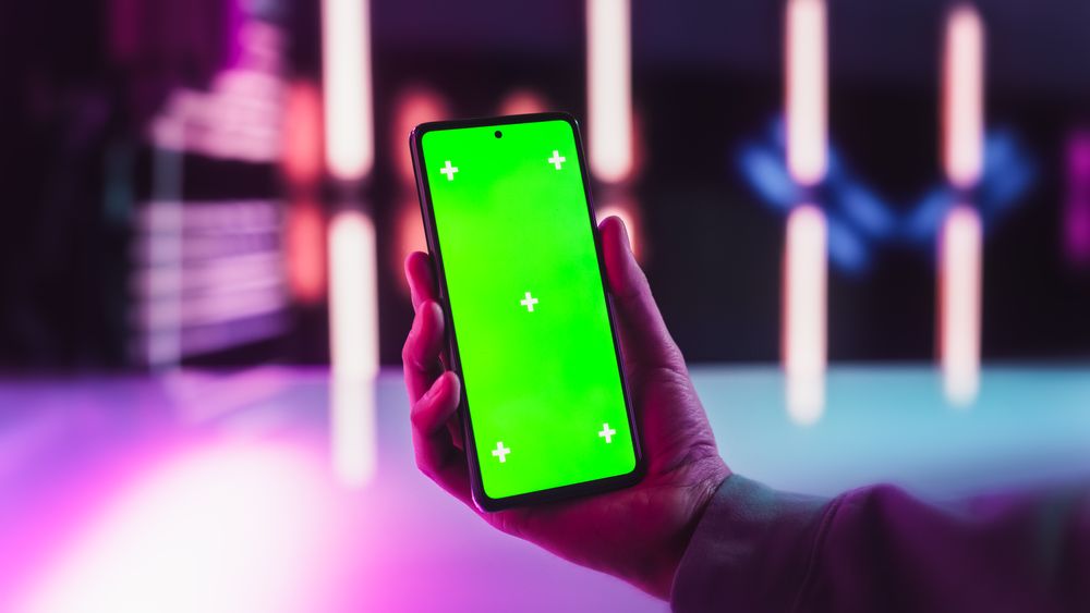 Anonymous Man Holding a Smartphone with Mock Up Green Screen Chromakey Display in a Futuristic Room with Neon Lights. Photo Template with Placeholder for Tech Advertising and Entertainment Content