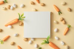 Easter eggs and carrots on pastel yellow background with paper card note