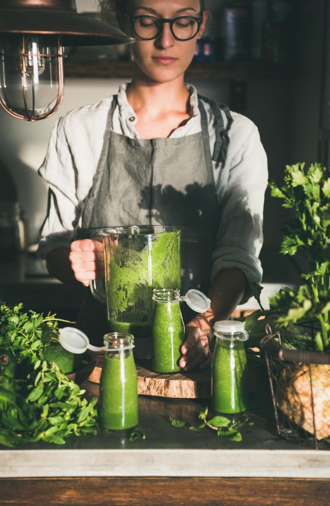 Woman with pitcher and three glass containers of green smoothie