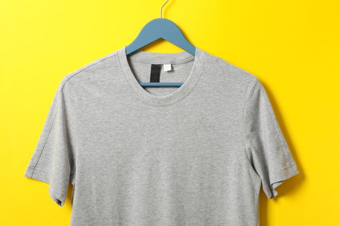 Hanger with blank gray t-shirt on yellow background, space for text