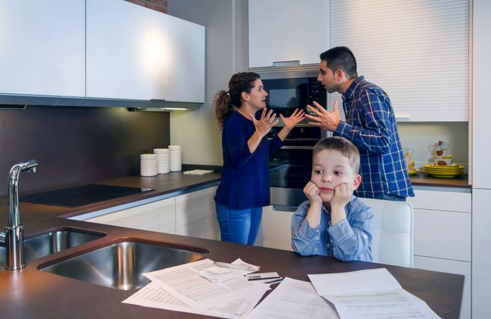 Couple arguing in front of son with bills scattered on the kitchen counter