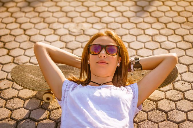 Young girl with a skateboard lying on the street in summer