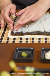Hands of woman chef flattening rice to roll sushi in a nori seaweed sheet, vertical 0L6OE4