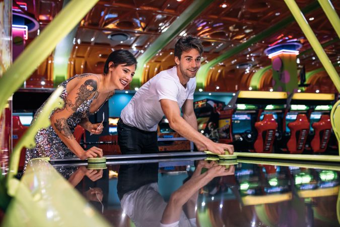 Happy couple playing coin operated air hockey game as a team in a gaming arcade