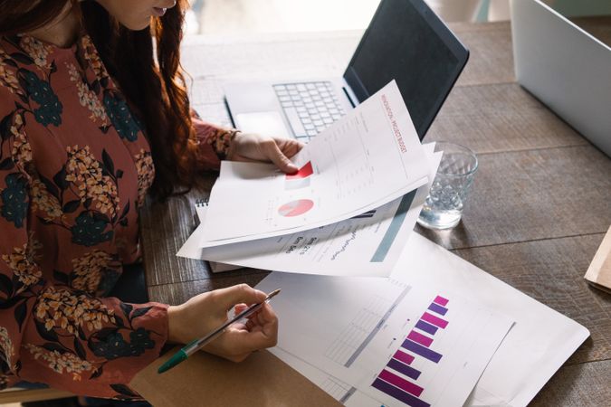 Crop serious woman analyzing financial report and sitting at desk