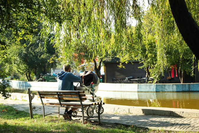 Man with stroller sitting on bench in city park
