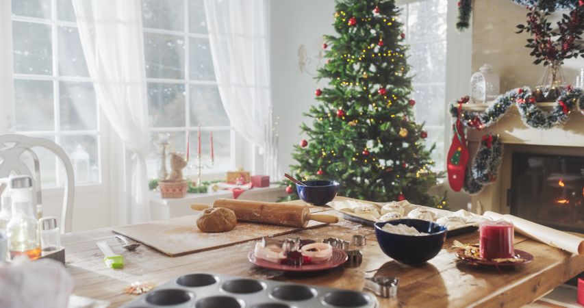 Peaceful Snowy Christmas Morning: Table with Baking Ingredients and Utensils in a Decorated Corner of a Modern House with a Christmas Tree, Fireplace and Gifts.