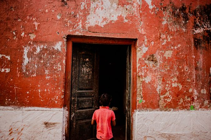 Back view of boy in red shirt standing in front of brown wooden door