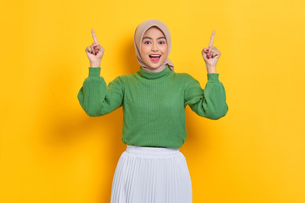 Surprised woman in headscarf holding up both fingers with good idea
