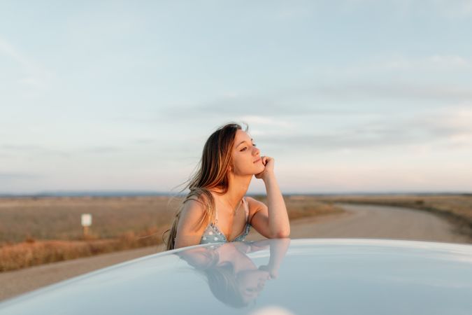 Young woman resting her head on her chin on roof of car