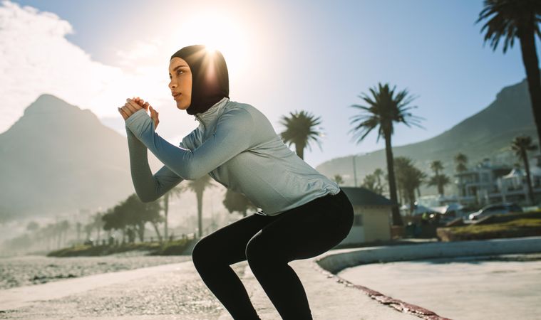 Fit woman in headscarf doing squats outdoors in morning