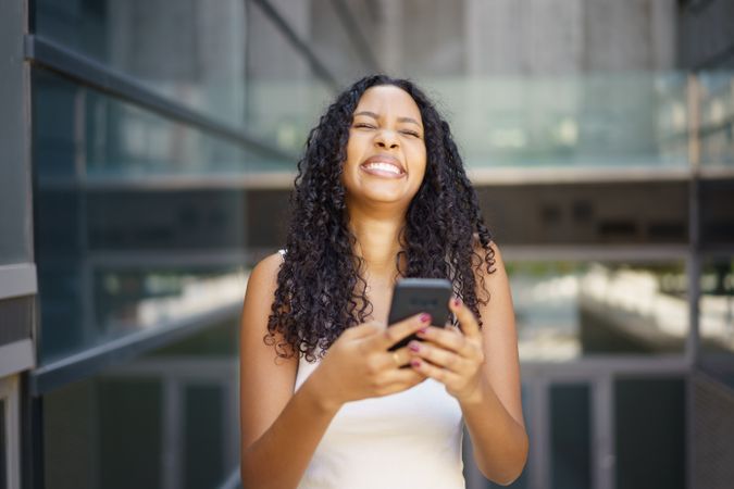 A Joyful Young Woman Enjoying Her Time Engaged with a Smartphone Outdoors in Daylight