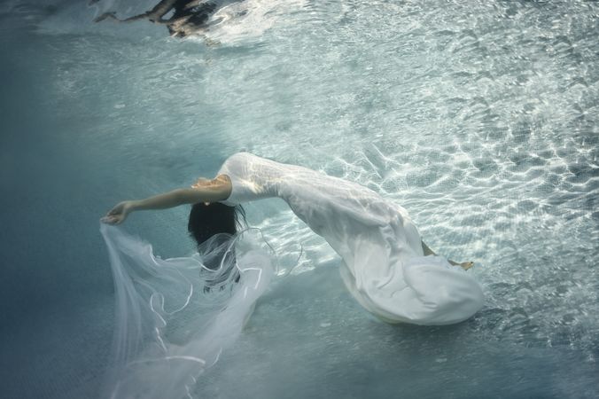 Woman in wedding dress floating underwater