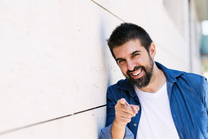 Man in denim standing outside smiling and pointing at camera