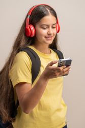 A happy young student smiling while listening to music on red headphones.