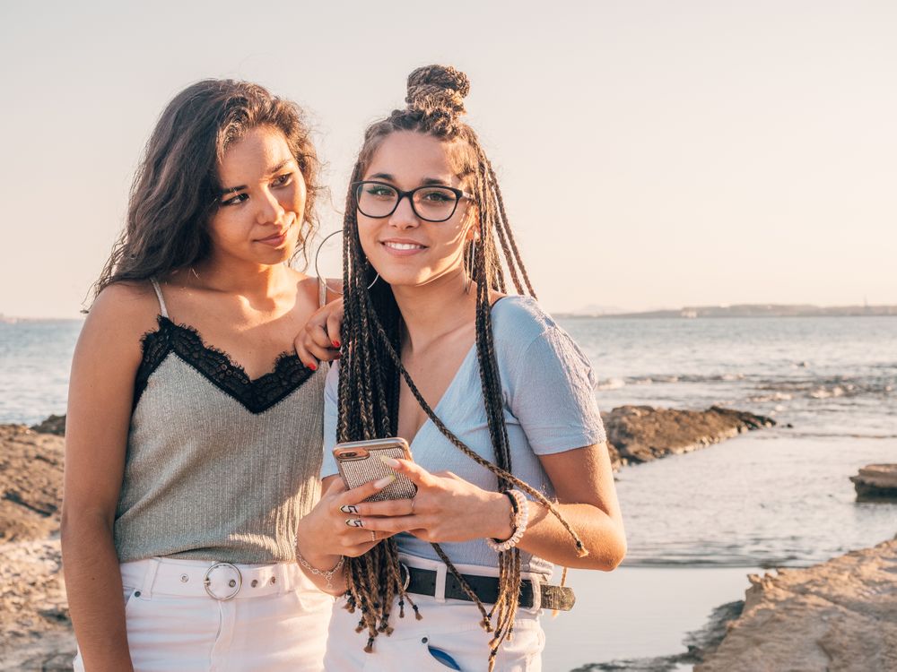 Smiling trendy young women using smartphone on beach