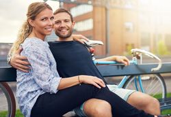 Couple smiling at camera while sitting on a city bench