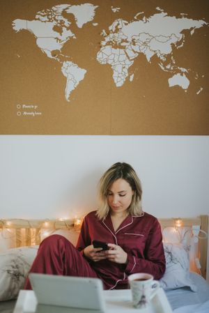 Woman sitting in bed with tablet and looking on smartphone