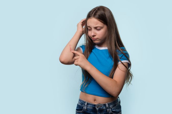 Young girl examining cut on elbow, looking concerned