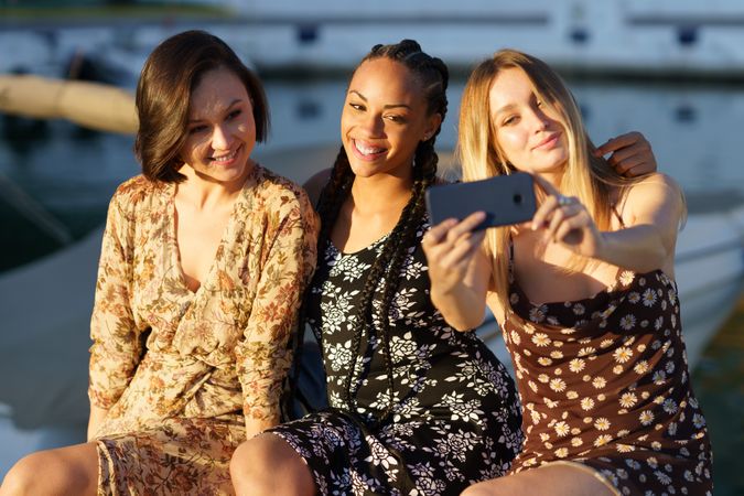 Three women sitting near coast taking selfie