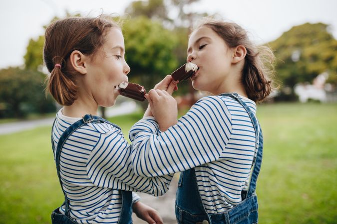 Identical twins sharing ice cream in the park