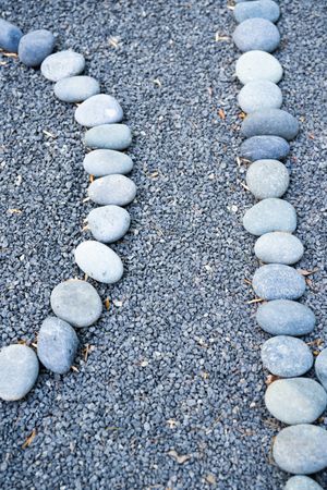 Small river rocks in curved lines on top of small pebbles in garden