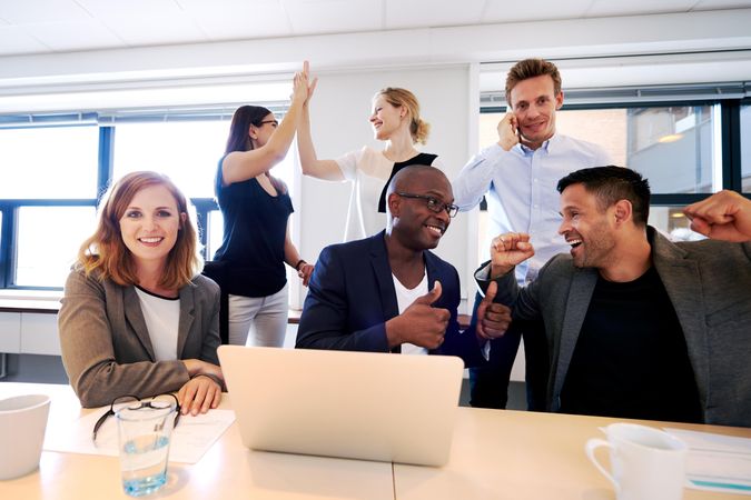 Business associates celebrating around a laptop in an office