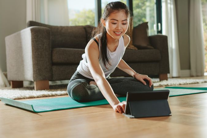 Smiling woman sitting exercise mat and watching training videos on digital table