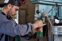 Male mechanic operating drilling machine in workshop