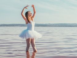 Ballerina in swimsuit with tutu performing classical position in water