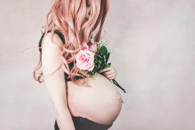 Side view of pregnant woman wearing dark bra holding pink rose bouquet