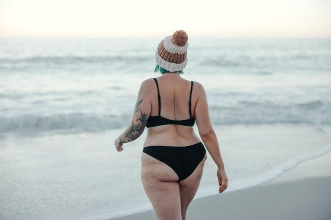 Rearview of female winter bather walking towards the water at the beach
