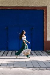 Young happy trendy woman walking in city against blue door
