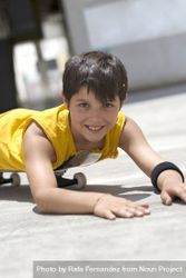 Young smiling boy lying on a skateboard while looking camera on a bright day 0V6wxr