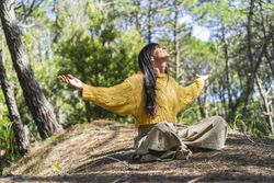 Woman sitting on the woods with arms opened while looking to the sky like thanking God