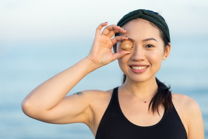 Happy Asian woman covering eye with sea shell