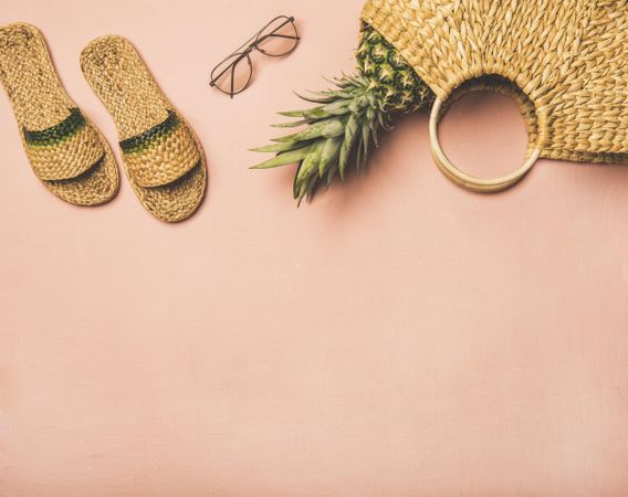 Sandals, glasses, pineapple in wicker bag, on pink background, with copy space