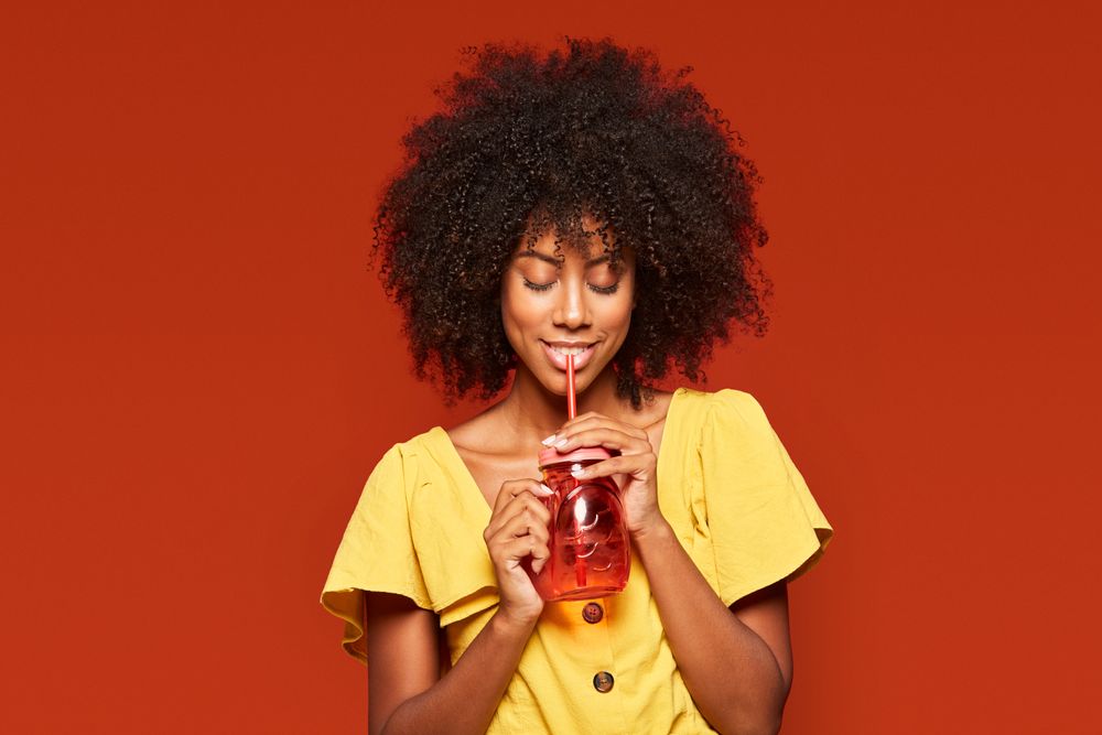 Charming bright Black woman drinking beverage