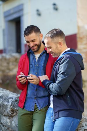 Two men smiling at something over a phone, vertical