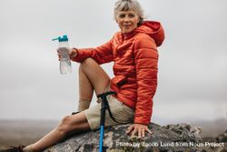 Mature woman sitting on a rock and drinking water 4NmXg5