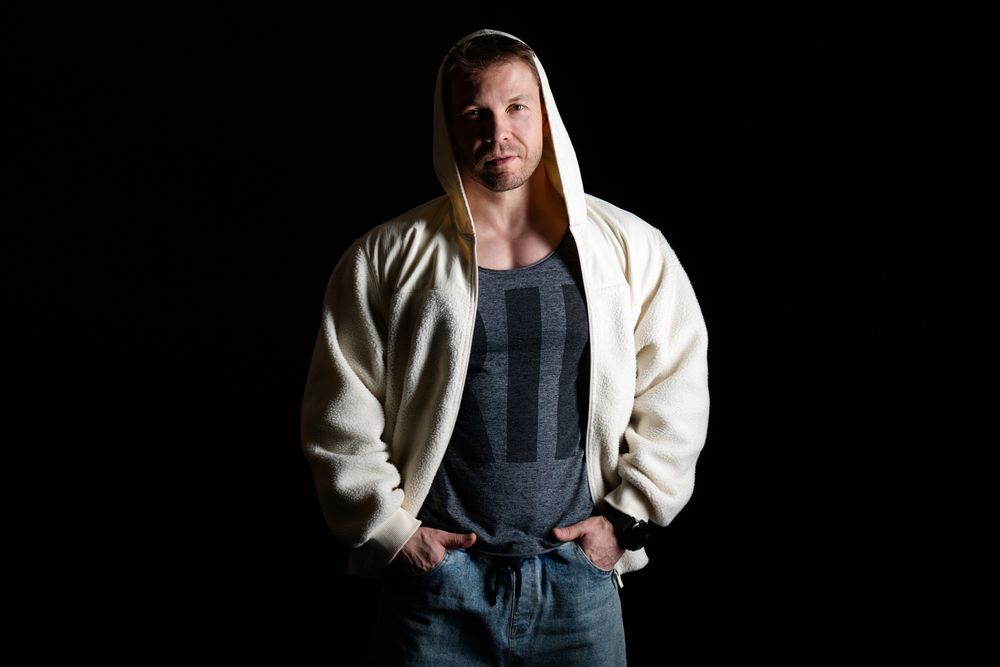 Man in hooded fleece jacket and jeans, hands in pockets.